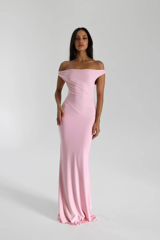 A woman in a pink, sleeveless, off-the-shoulder, maxi dress by Natalie Rolt with a structured neckline.