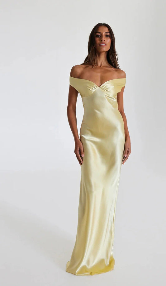 A woman wearing a Nalatlie Rolt off-shoulder, full-length yellow silk dress with a bias-cut silhouette, featuring gathered bust cups and an elasticated back.