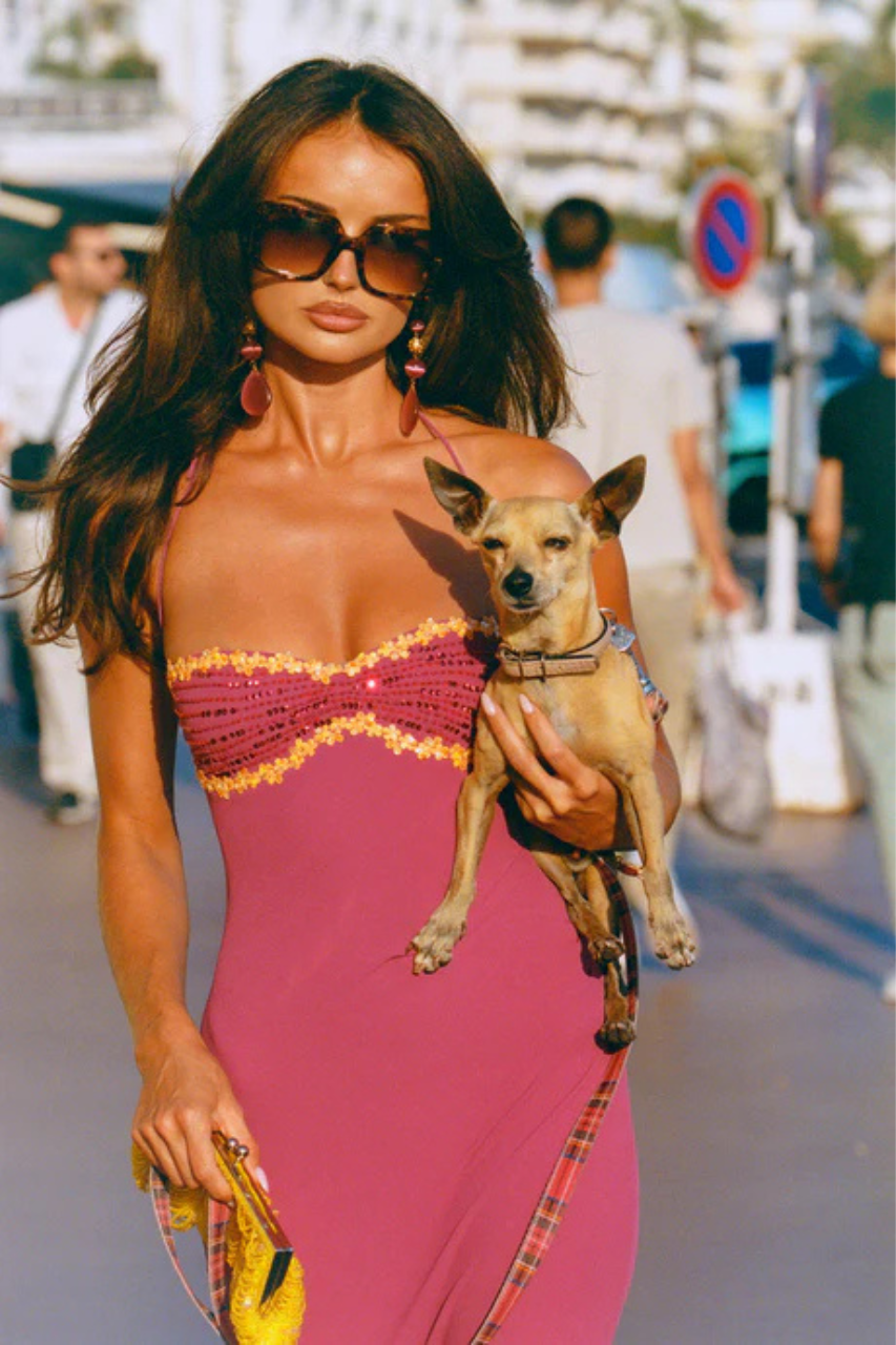Woman in a I am Delilah Maxi Wine dress holding a small dog on a city street.