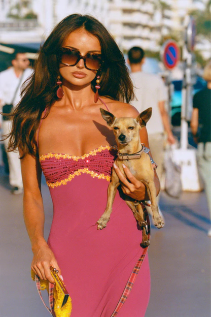 Woman in a I am Delilah Maxi Wine dress holding a small dog on a city street.